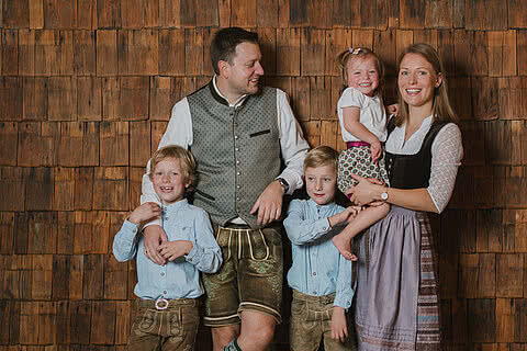 Familie Hettegger posiert in traditioneller Tracht vor einer rustikalen Holzwand im Tauernhof in Großarl