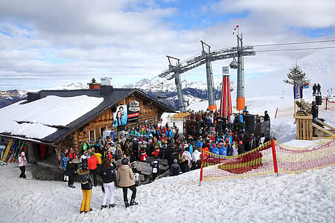 Eine lebhafte Après-Ski-Atmosphäre vor einer Berghütte während der Lady-Skiwoche, umgeben von verschneiten Bergen. Gäste des Hotel Tauernhof in Großarl können dieses Event hautnah erleben.
